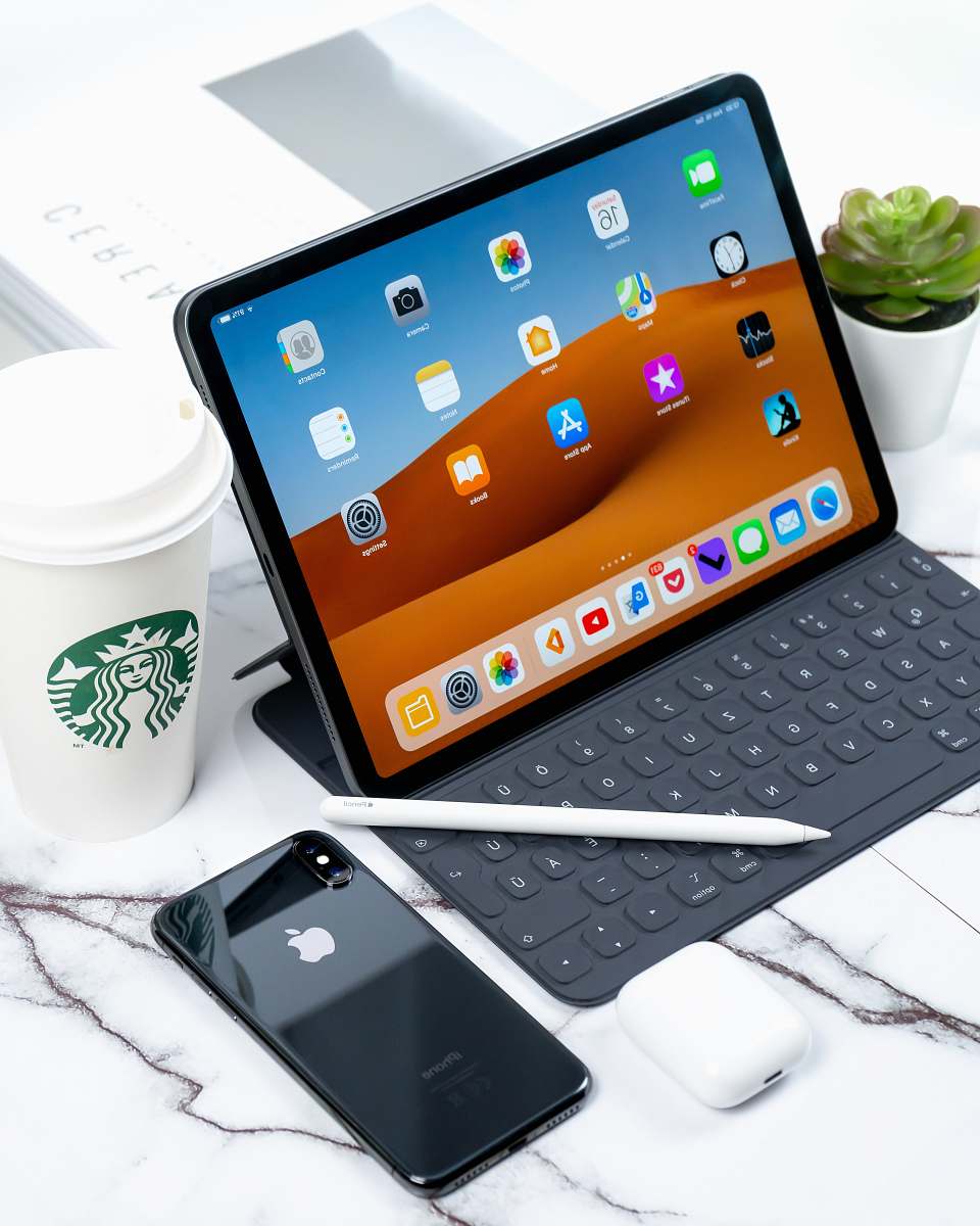 mobile phone turned on iPad beside space gray iPhone X and Starbucks coffee cup cell phone